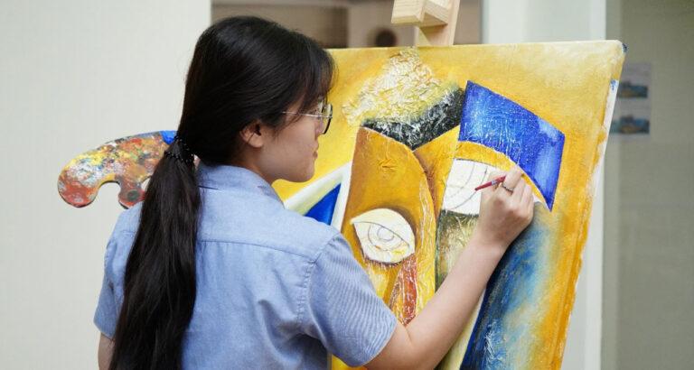 A student from Prometheus School Secondary is creating artwork in the presence of a live audience consisting of parents