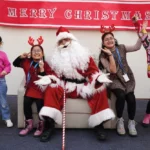 Santa Claus spreading joy, posing with cheerful students at the festive gathering. A heartwarming moment capturing the holiday spirit and excitement during the special event at the school.