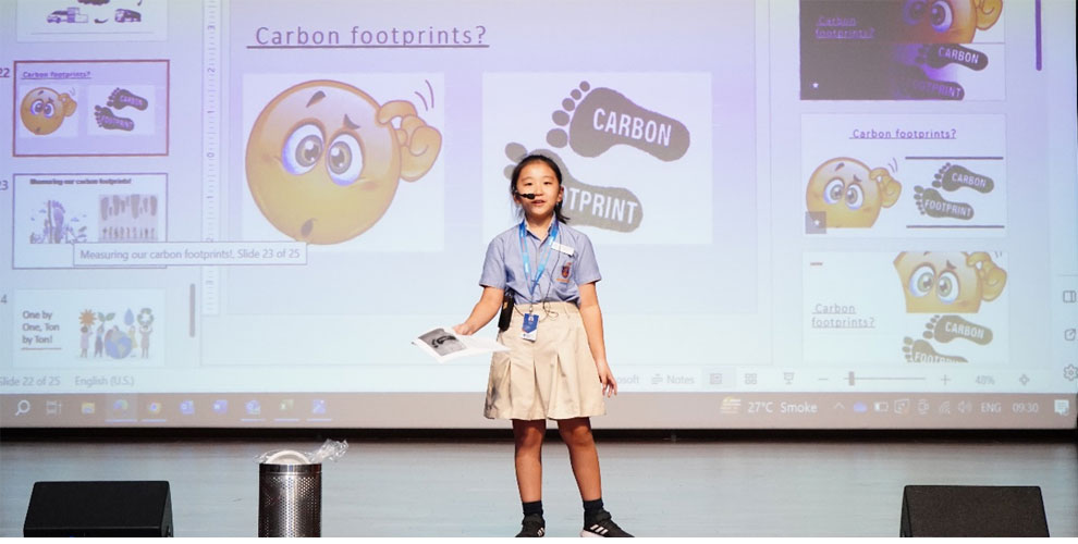 A girl is giving a presentation on carbon footprints, educating her peers on the importance of reducing individual and collective environmental impact at Prometheus School