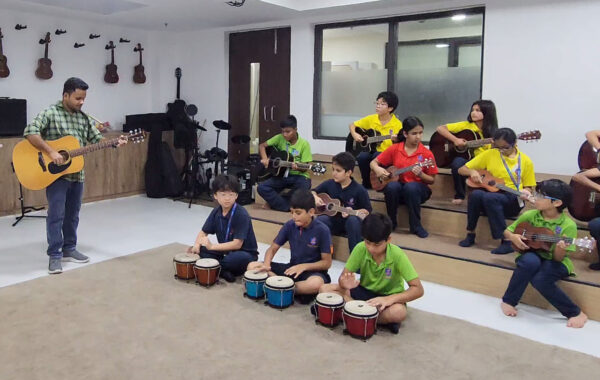A group of students playing various instruments like ukulele and guitar alongside their teacher during a music session