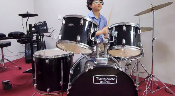 A student skilfully playing a drum set in the music room at Prometheus School, focusing on rhythm and beats