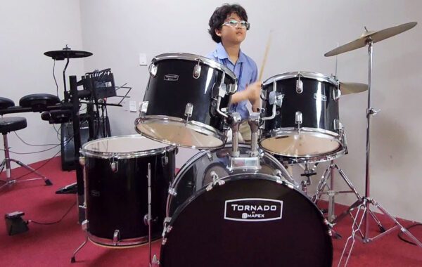 A student skilfully playing a drum set in the music room at Prometheus School, focusing on rhythm and beats
