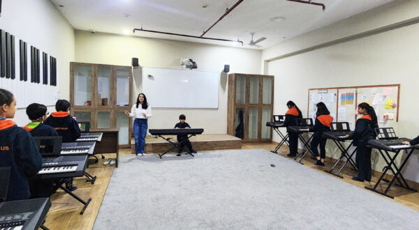 A teacher giving a keyboard lesson in the music class, demonstrating techniques to attentive students