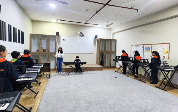 A teacher giving a keyboard lesson in the music class, demonstrating techniques to attentive students