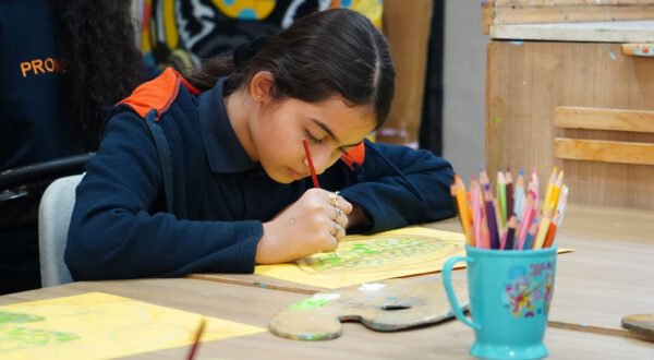 Prometheus School girl calmly painting with focus, surrounded by a colour palette, pencil colours, and art supplies, showcasing a serene moment of creativity