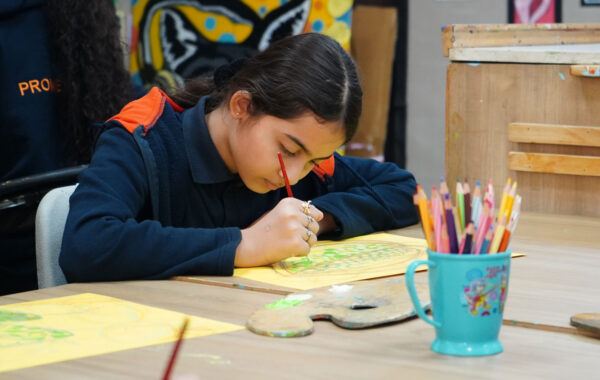 Prometheus School girl calmly painting with focus, surrounded by a colour palette, pencil colours, and art supplies, showcasing a serene moment of creativity