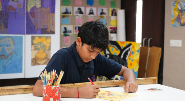 Prometheus School student painting and colouring his artwork, with vibrant paintings displayed in the background and art supplies like paints and brushes spread on the table