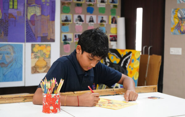 Prometheus School student painting and colouring his artwork, with vibrant paintings displayed in the background and art supplies like paints and brushes spread on the table