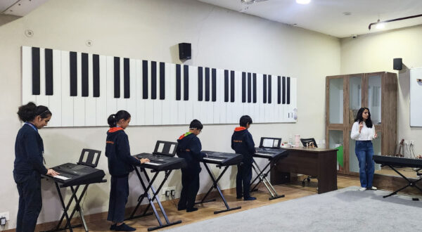Students practicing on keyboards in the music room while their teacher guides and instructs them