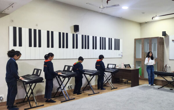 Students practicing on keyboards in the music room while their teacher guides and instructs them