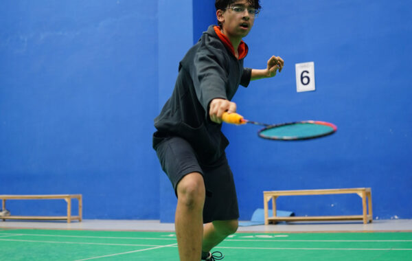 Defending-A Prometheus School student leans forward with determination, defending against the opponent's shuttlecock during a thrilling match