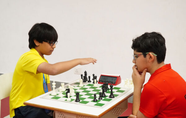 Prometheus Topaz house student moves a chess piece while the Ruby house student considers their next strategic move