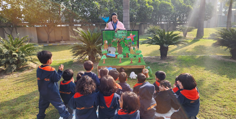  Learning Through Play – A teacher captivates young learners with an engaging story session in an outdoor setting, using a story sack to bring the tale to life while students listen attentively and enjoy the experience.