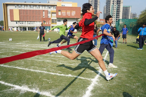 Students sprint to the finish line in a school race, with one breaking the ribbon as others follow closely.