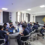 Students working on laptops and tablets in a modern robotics lab, surrounded by technology-themed decor with words like 'innovation' and 'creativity' on the walls