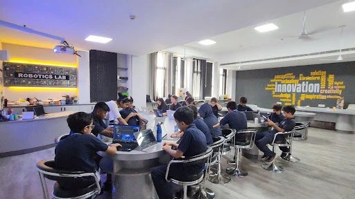 Students working on laptops and tablets in a modern robotics lab, surrounded by technology-themed decor with words like 'innovation' and 'creativity' on the walls